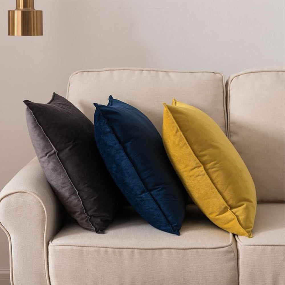 Three colorful pillows (gray, blue, yellow) on a beige sofa against a neutral wall.
