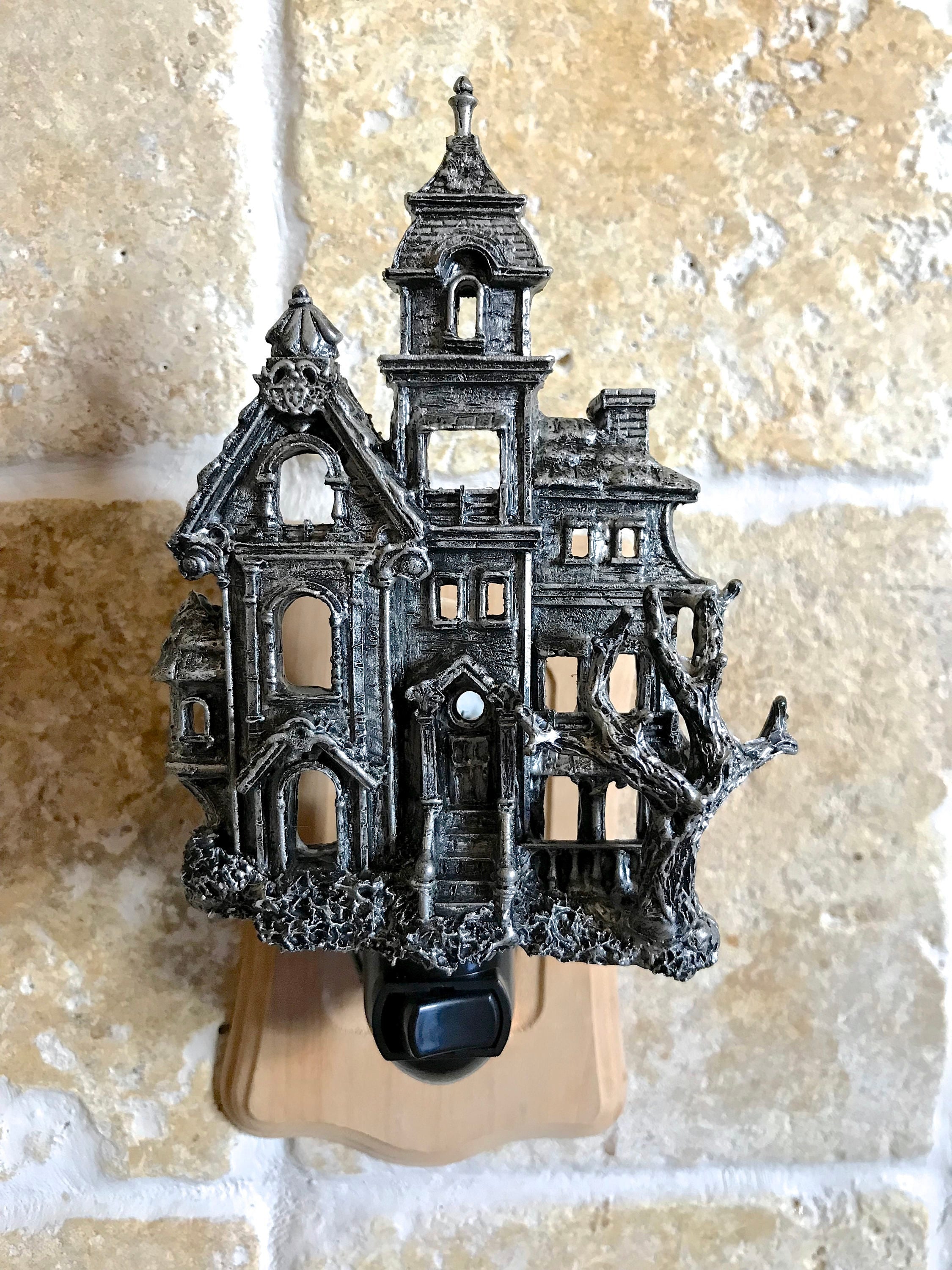 Decorative night light shaped like a haunted house on a textured wall.