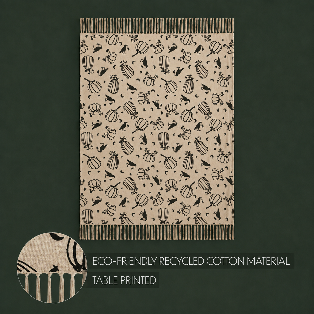 A rectangular tablecloth with a beige background and a black printed pattern of pumpkins, birds, and autumn leaves, shown on a dark green background. A circular inset at the bottom left shows a close-up of the pattern and fringed edges.