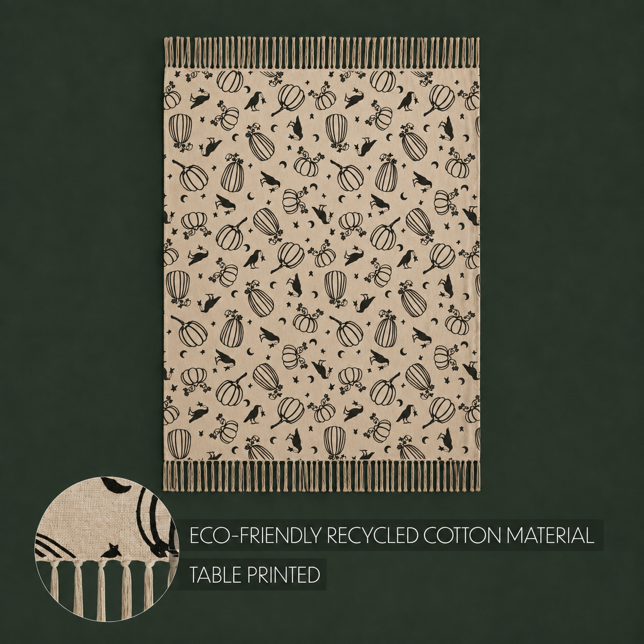 A rectangular tablecloth with a beige background and a black printed pattern of pumpkins, birds, and autumn leaves, shown on a dark green background. A circular inset at the bottom left shows a close-up of the pattern and fringed edges.