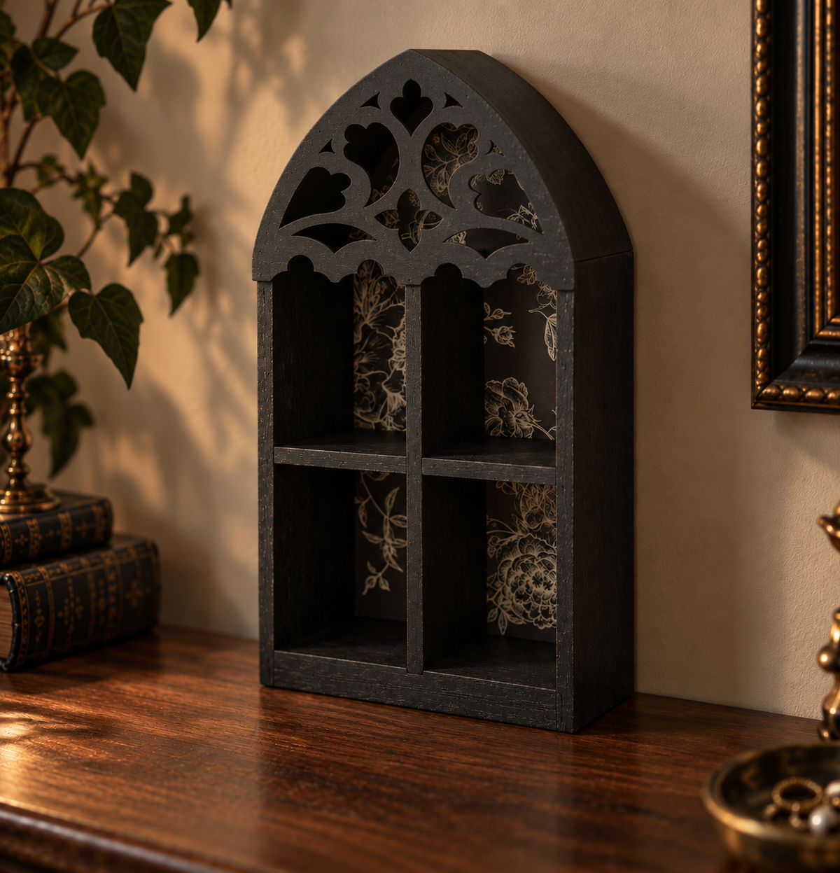 A black arched Gothic-style wall shelf with four open compartments and floral-patterned interior panels, displayed on a wooden table against a beige wall.