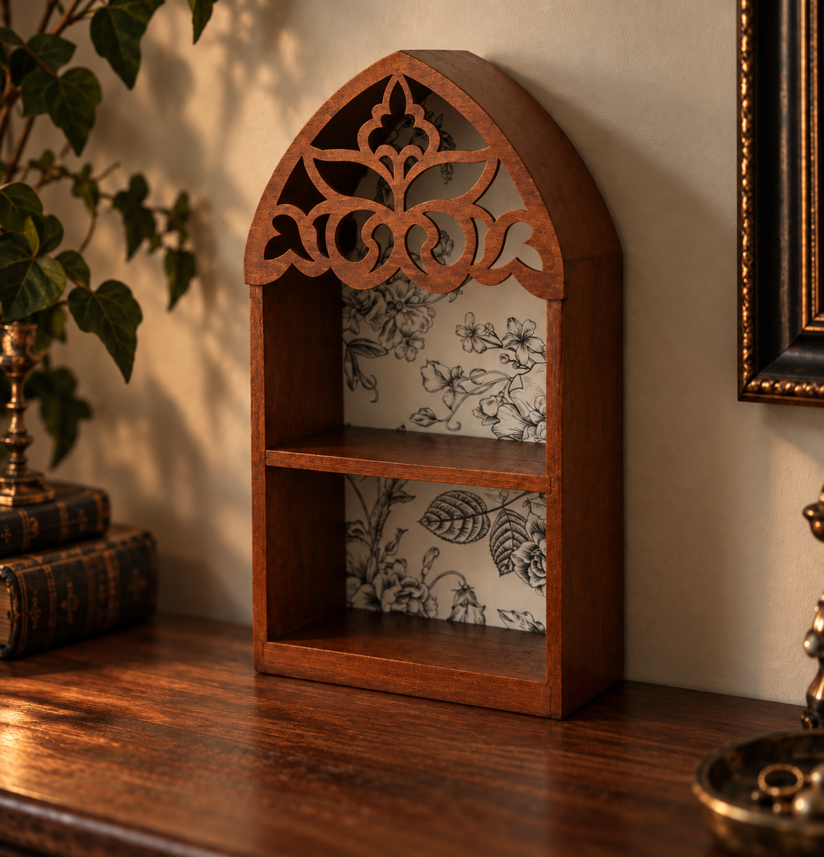 A small arched wooden shelf with ornate cutout detailing at the top and two open shelves, shown on a wooden table in a styled interior setting.
