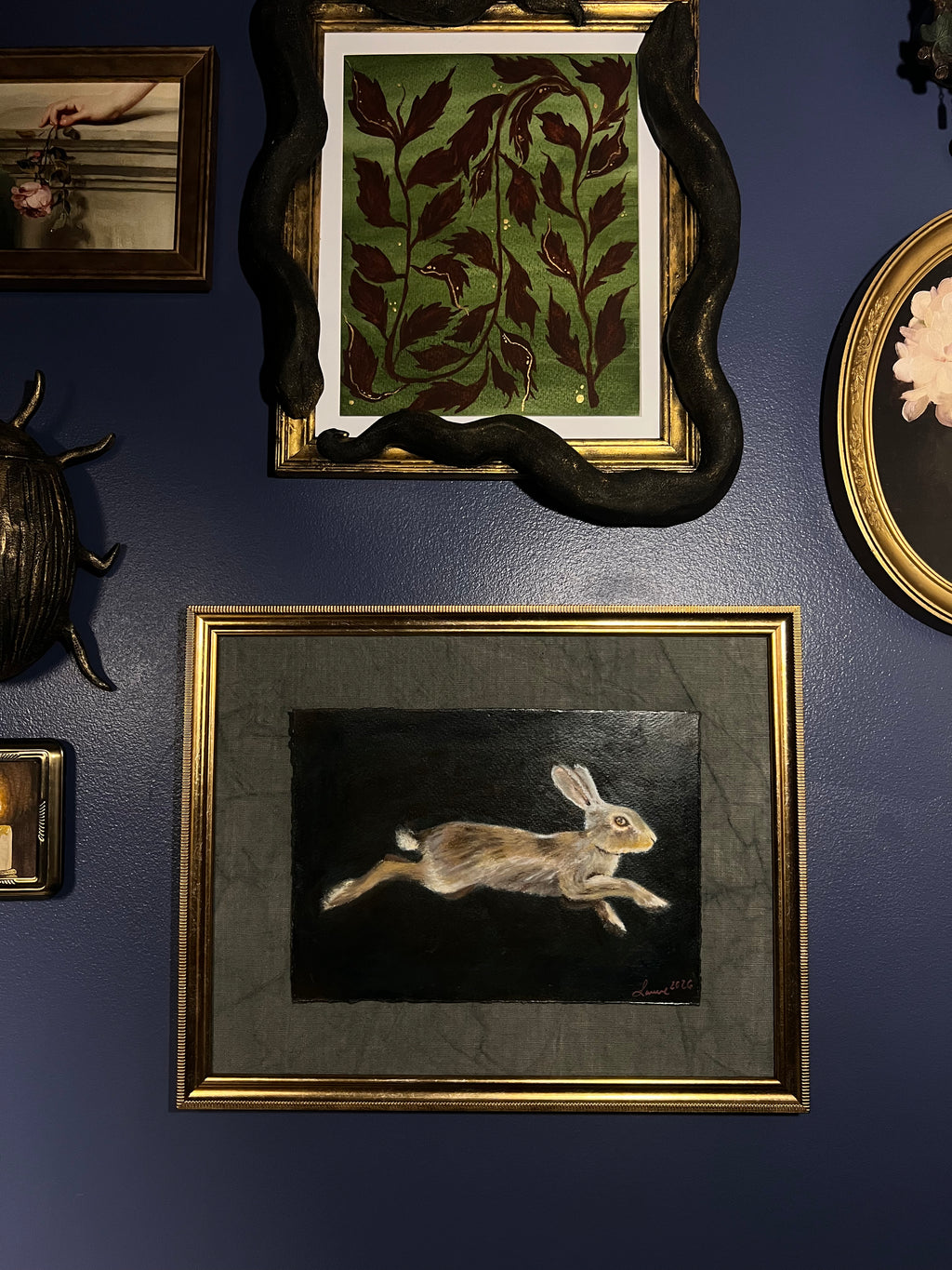A framed art print depicting a leaping rabbit on a dark background, mounted on a dark blue wall alongside other decorative frames and objects.