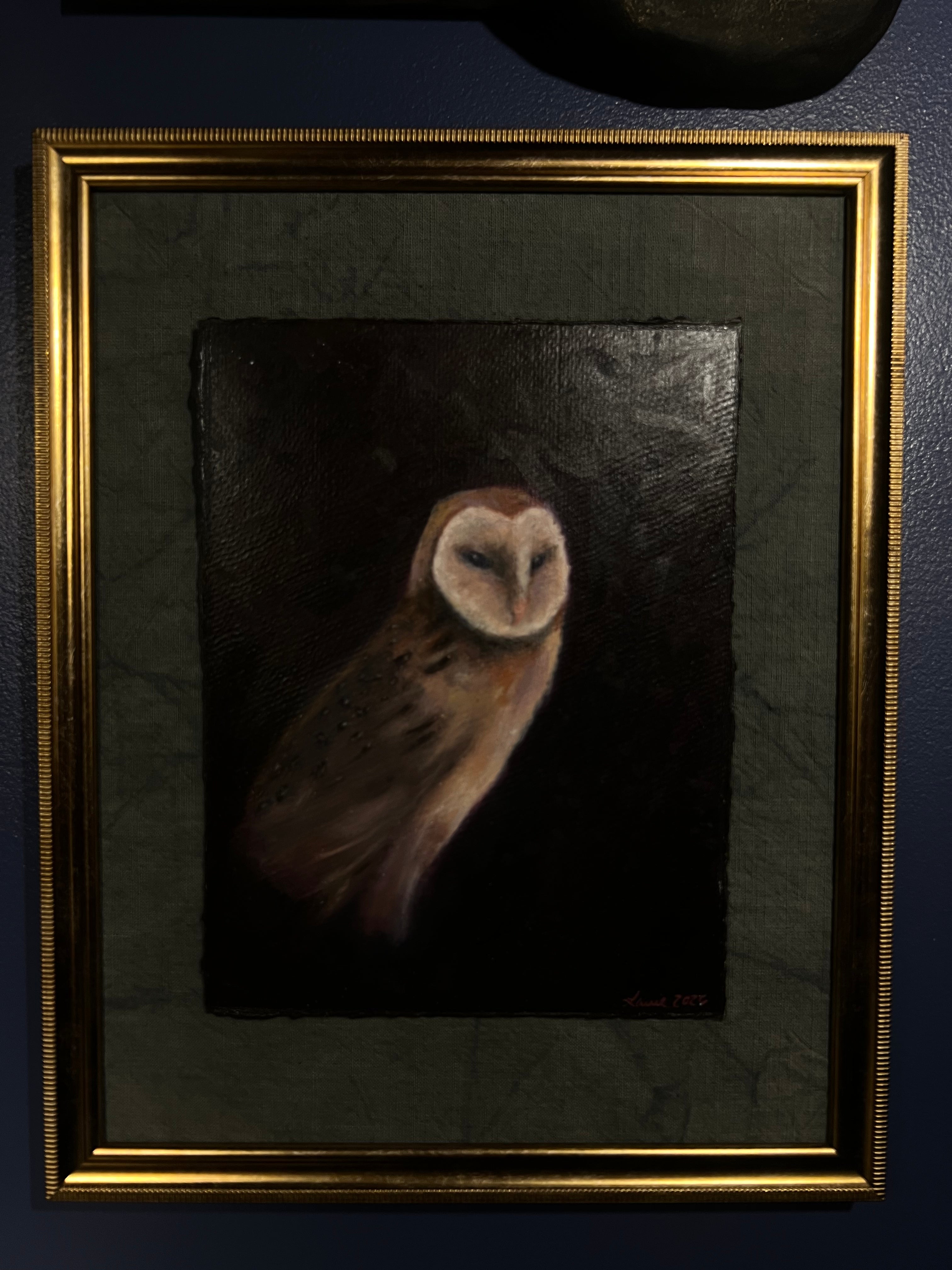 A framed oil painting of a barn owl on a dark background, featuring a textured dark green mat and a gold frame, mounted on a dark blue wall.