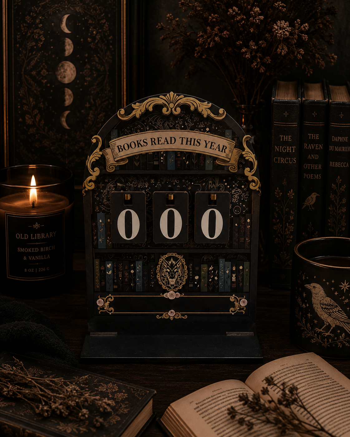An ornate vintage-style book year calendar on a dark wooden table surrounded by books, a lit candle, and dried flowers. The calendar has gold detailing and the text 'BOOKS READ THIS YEAR' above rotating numerals showing '000'.