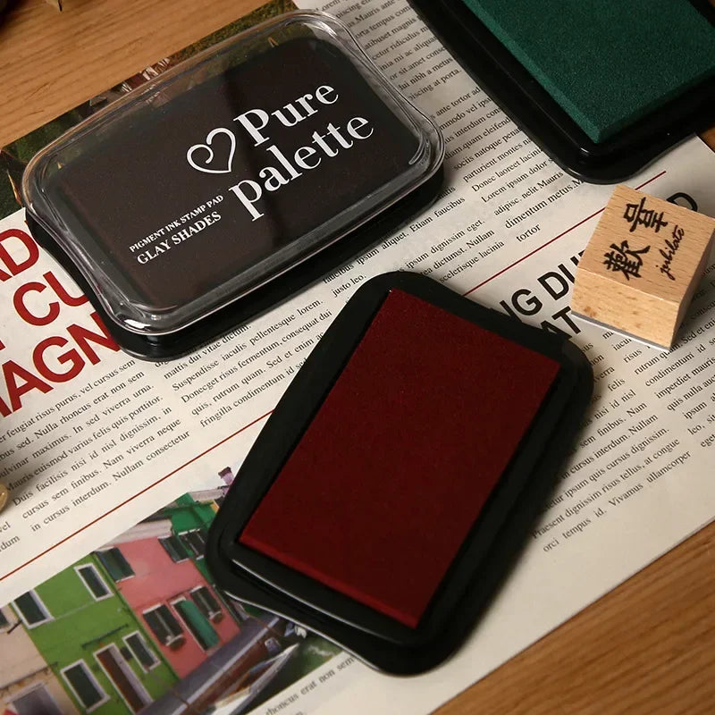 Two ink pads, one black and one red, on a newspaper background with 'Pure Palette' branding.