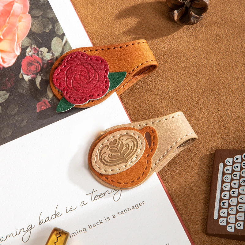 Two leather bookmarks with floral designs on a textured surface.