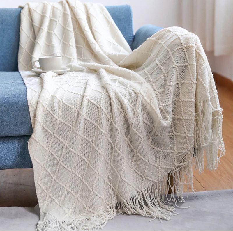 White textured throw blanket draped over a blue sofa with a cup on top.