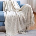 White textured throw blanket draped over a blue sofa with a cup on top.