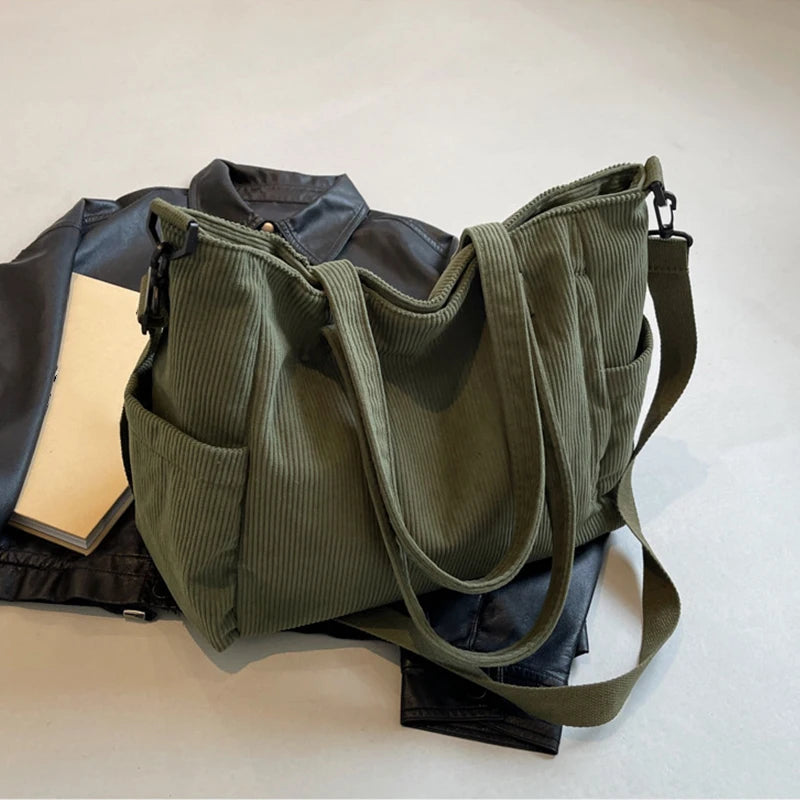 Green tote bag with a black jacket and gold book on a light background