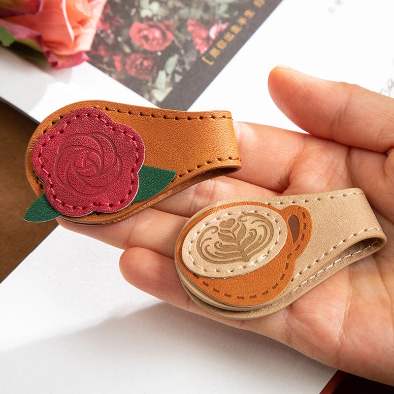 Hand holding two leather keychains with floral designs on a white surface.