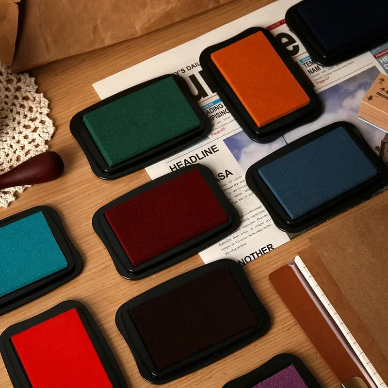 Collection of colorful stamp ink pads on a wooden surface with newspaper underneath