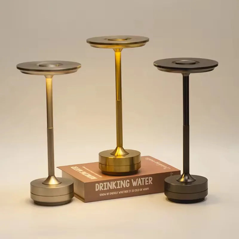 Three metallic candle holders on a beige background with a book titled 'Drinking Water'.