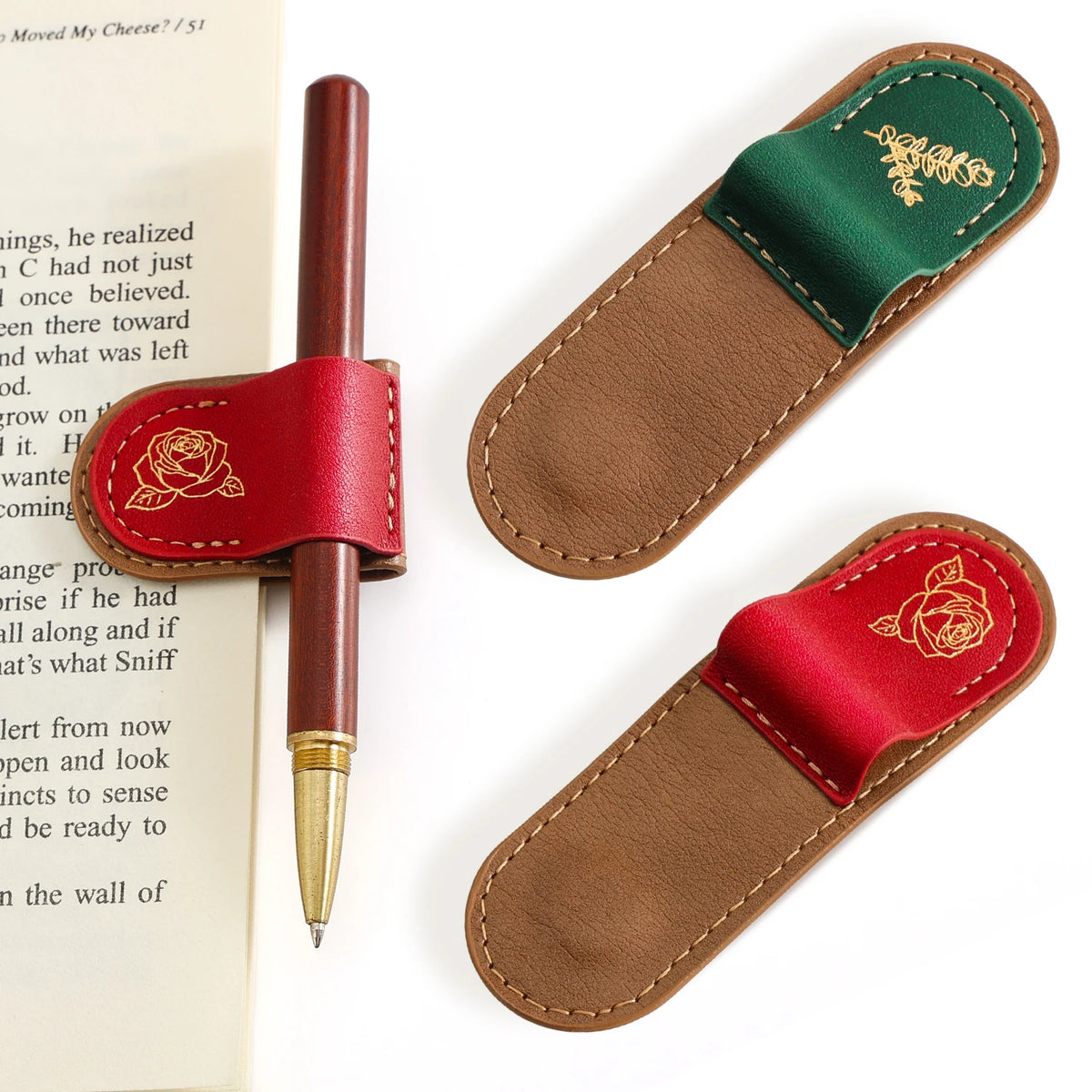 Two leather pen loops shown on a white background, one attached to a brown pen and one empty, both with gold rose embroidery. A book page is visible on the left as a styled prop.