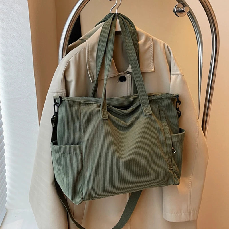 Green corduroy bag hanging on a hanger with a beige jacket in the background