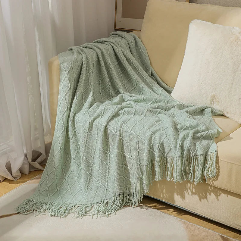 Light green textured throw blanket draped over a beige sofa with white cushions.