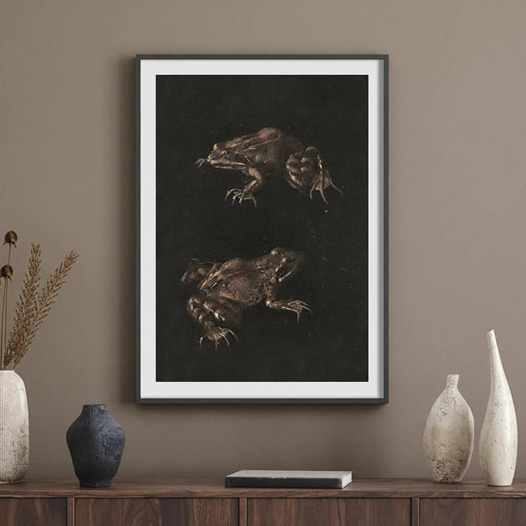 A framed art print featuring two detailed frog studies on a dark background, hung on a brown wall above a wooden console table with decorative vases.
