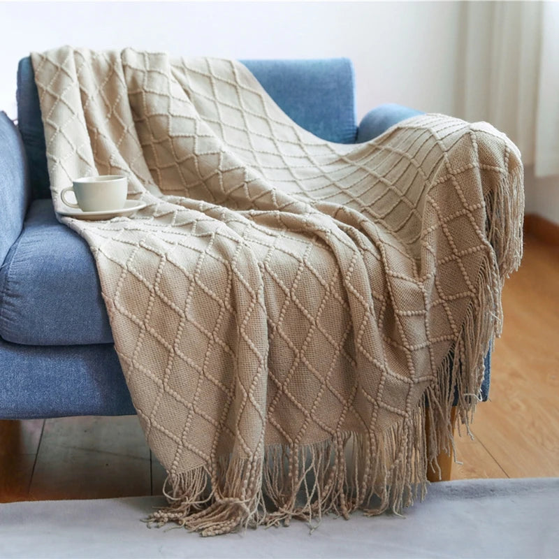 Beige diamond patterned throw blanket draped over a blue sofa with a cup on a small table.