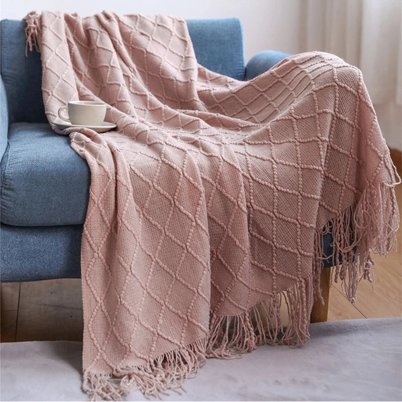 Pink textured throw blanket draped over a blue sofa with a white bowl on a wooden table.