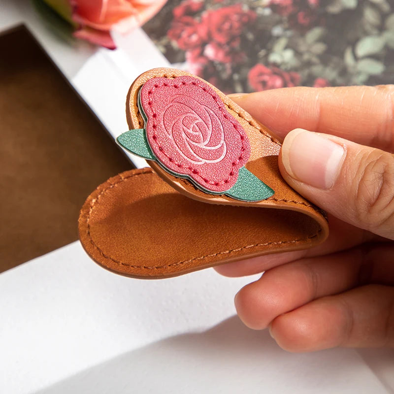 Hand holding a small leather item with a pink rose design on a white surface.