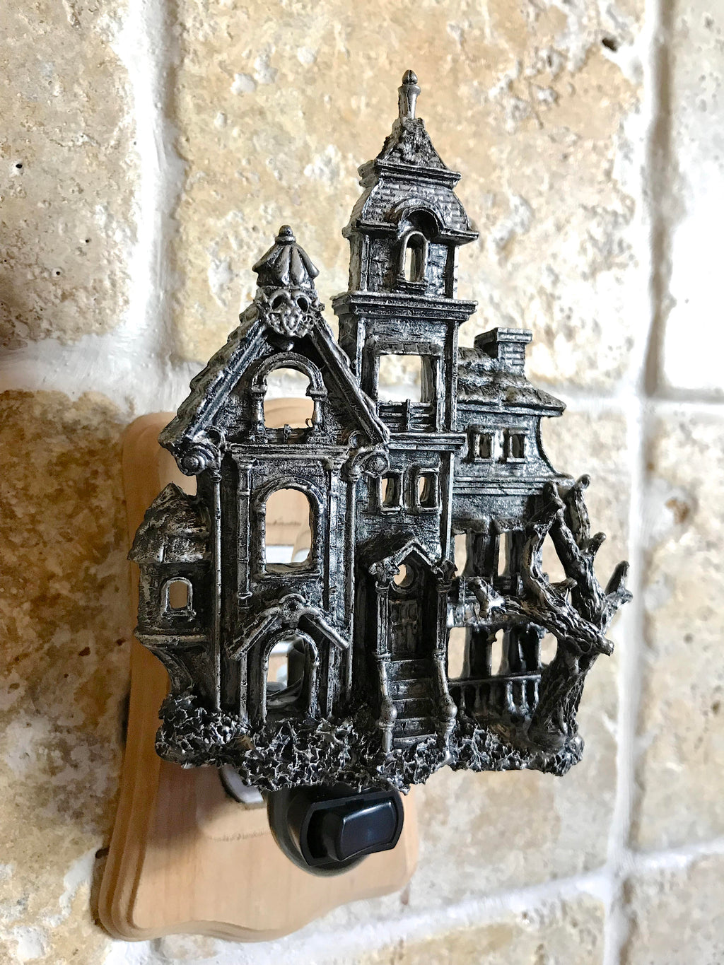 Decorative metal haunted house wall hook on a textured stone wall.