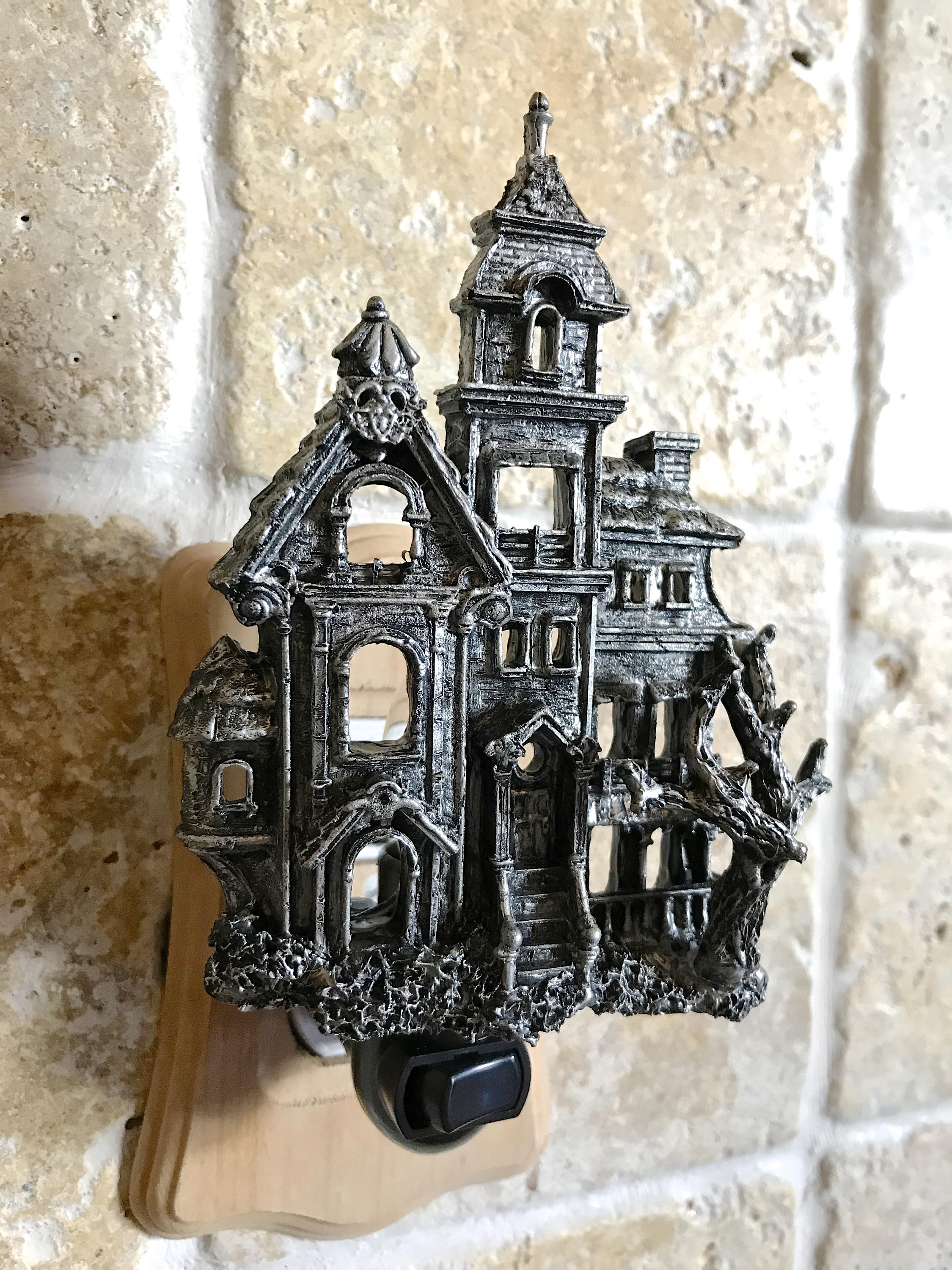 Decorative metal haunted house wall hook on a textured stone wall.