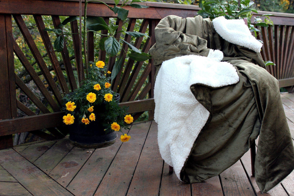 Chair with green cover and white blanket on a wooden deck with flowers nearby