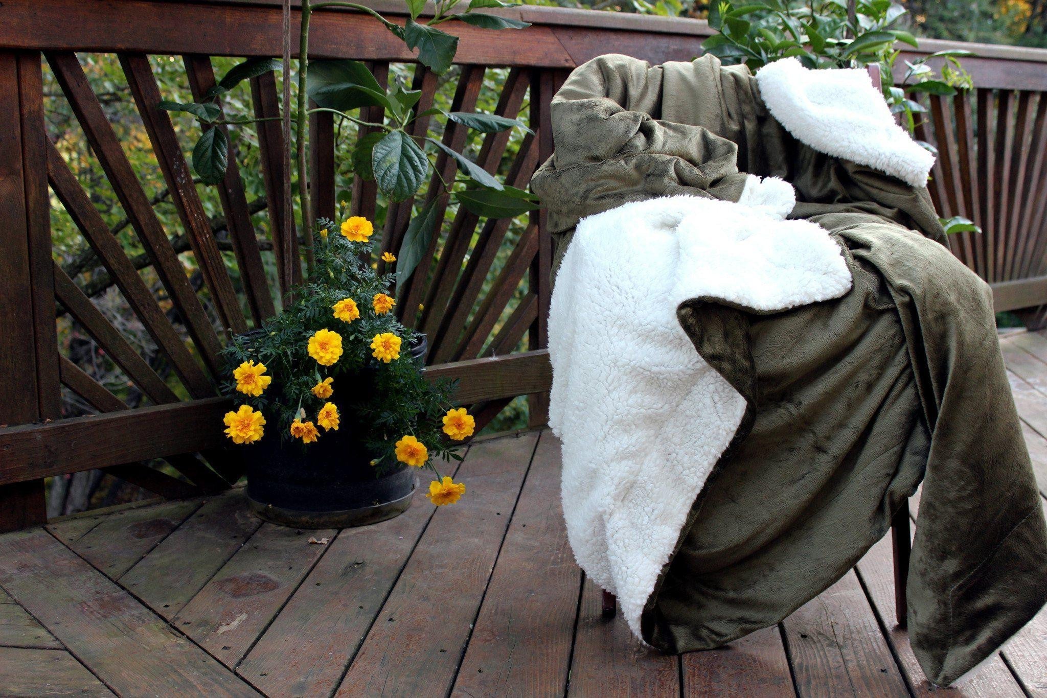 Chair with green cover and white blanket on a wooden deck with flowers nearby