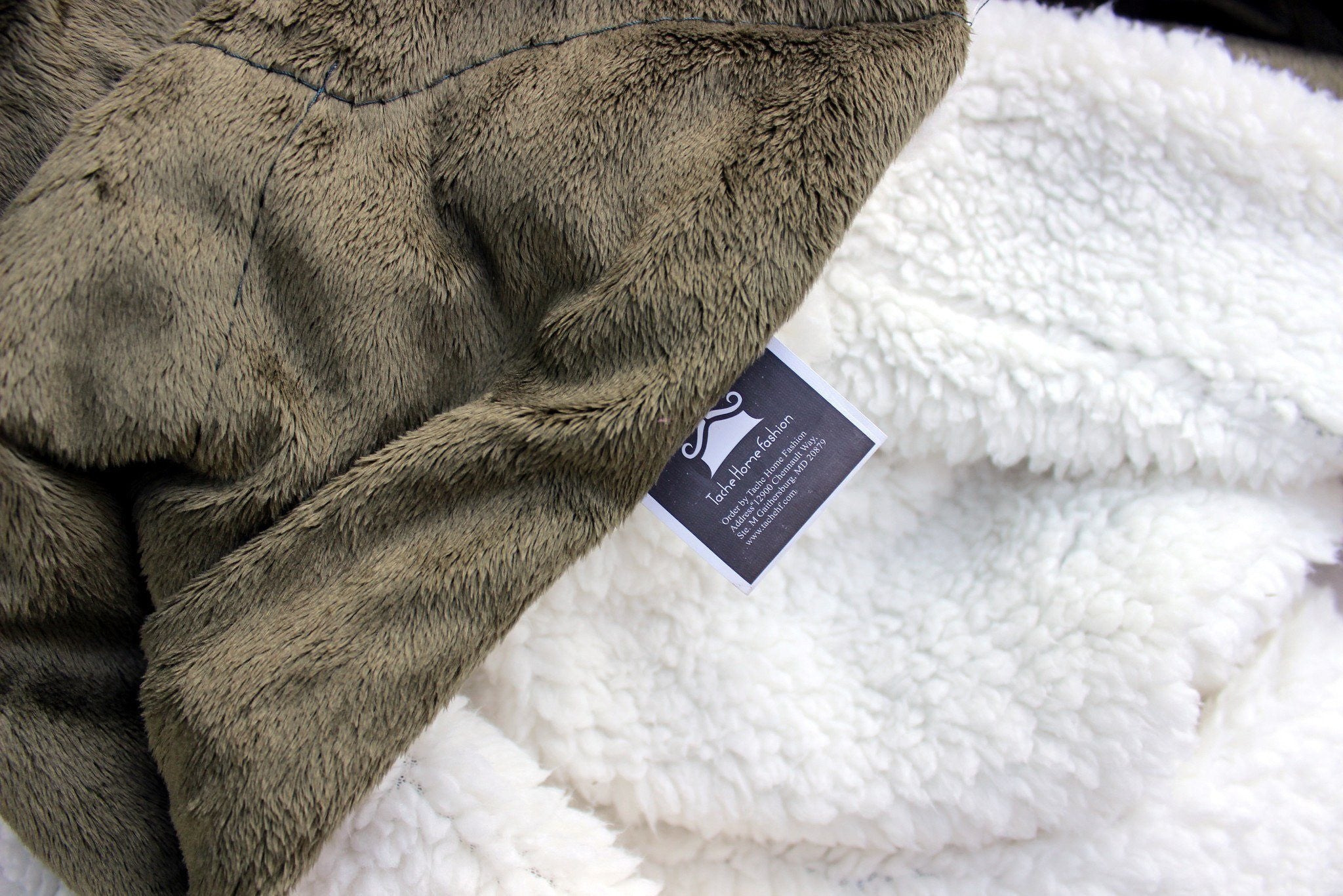 Close-up of a textured gray blanket with a brand tag on a white surface