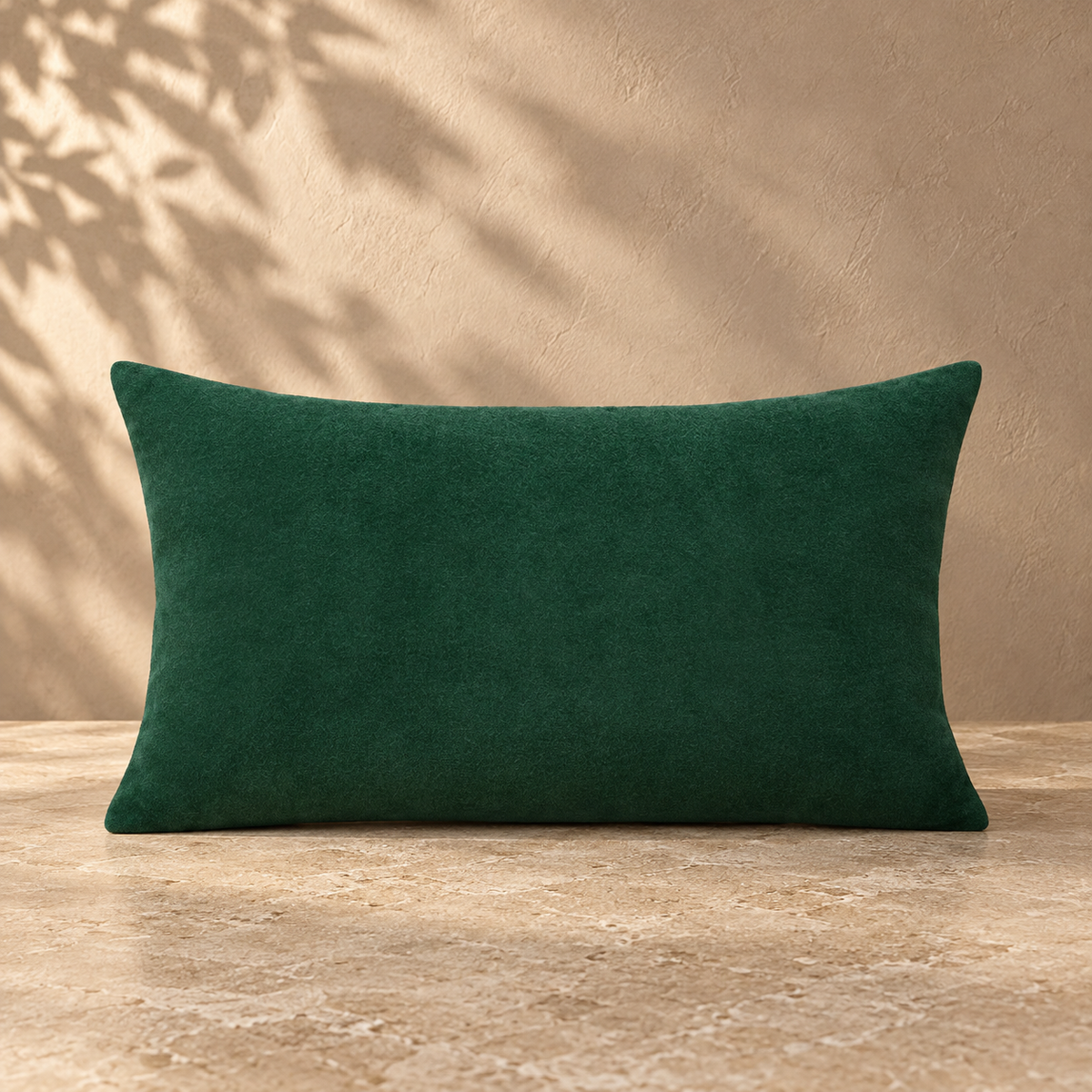 Green velvet lumbar pillow with plain edges against a warm plaster backdrop
