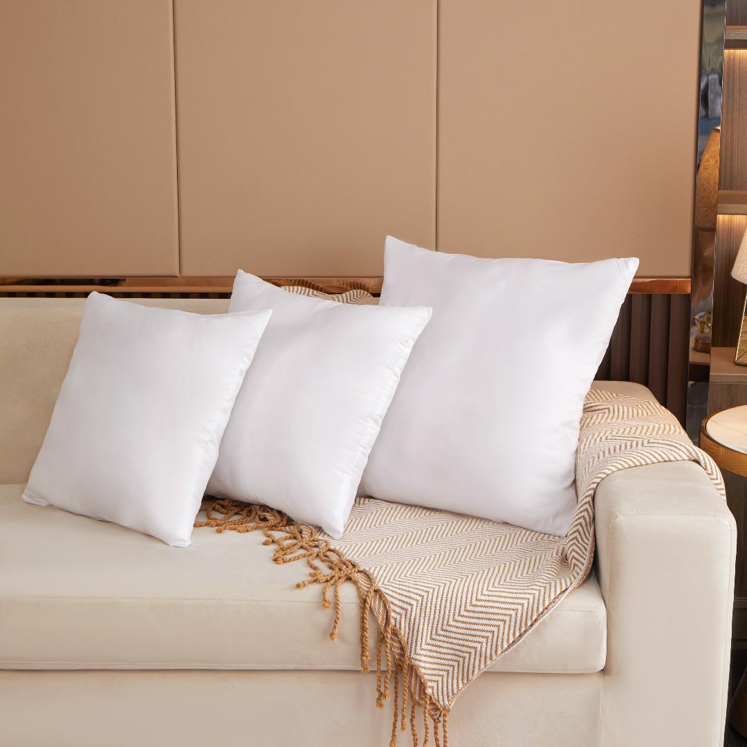 White pillows on a beige sofa with a textured blanket in a living room setting.