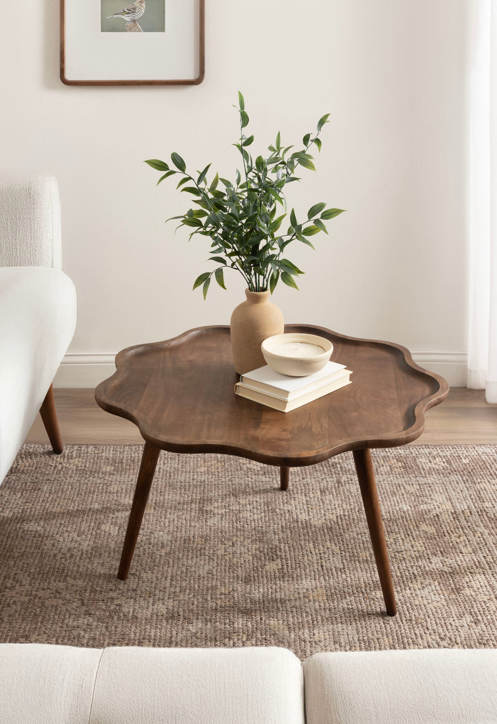 Wooden coffee table with a vase of greenery and books in a living room setting.